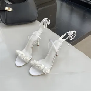 Detailaufnahme eleganter weißer Stiletto-Sandalen mit zartem Rosen-Blumenriemen