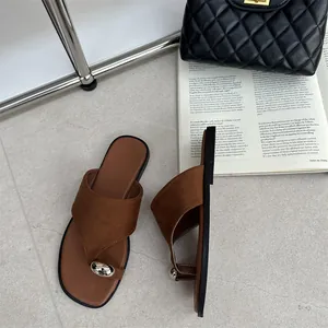 Detail van bruine suède teenslippers met zilveren ornament en zwarte gewatteerde tas