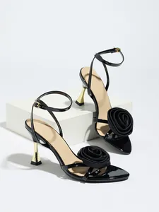 Detail of black satin sandals featuring a large fabric rose and gold flared high heel.