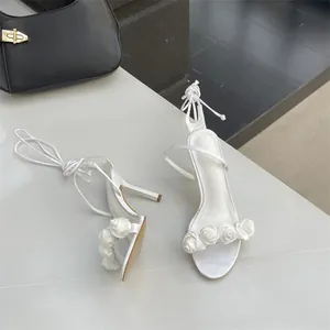 Detailansicht der weißen High-Heel-Sandalen mit Stoffrosen-Akzenten und Schnürbändern