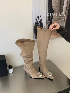 Detailed view of elegant beige pointed-toe boots featuring a luxury rhinestone buckle