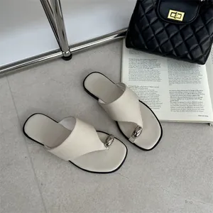 Detailopname van beige platte teenslippers met zilveren steen op grijze tegels