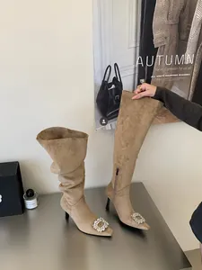 Detailed view of tan suede pointed-toe boots with sparkling crystal buckles