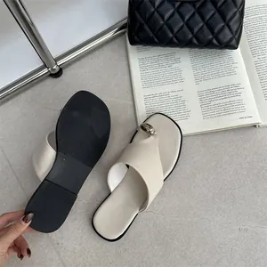 Detail van beige platte teenslippers met gouden gesp tegen een stijlvolle lifestyle-achtergrond