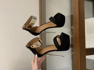 Detailed macro view of black platform stiletto sandals featuring a bold gold ankle strap