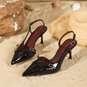 Elegante schwarze Lackleder-Slingpumps mit spitzer Kappe und Schnallen auf Strandsand