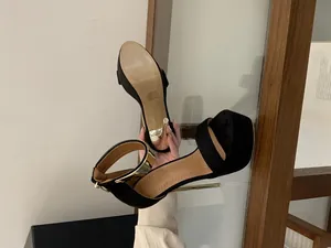Detailed view of black suede platform high heel sandals with gold metal buckle.