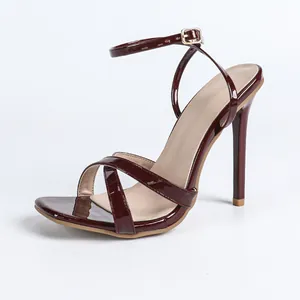 Vista lateral de elegantes sandalias de tacón de aguja en charol burdeos con tiras cruzadas