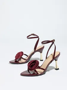 Detailed view of elegant wine red patent sandals featuring a satin rose and gold flared heel.