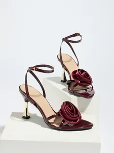 Detailed shot of elegant burgundy satin high heel sandals featuring a large fabric rose accent