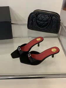 Detail of black square-toe mules with rhinestone buckles and red insoles.