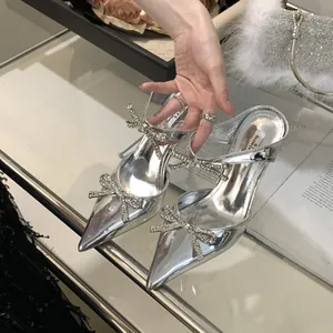 Detail shot of silver high-heeled sandals with elegant rhinestone bow accents.
