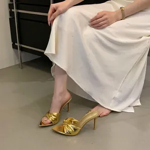 Detailansicht eleganter goldener Pantoletten mit gedrehtem Riemen, Pfennigabsatz und Spitze