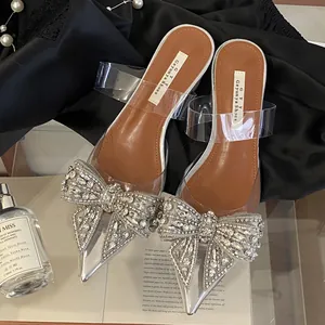 Detailansicht klarer PVC-Mules mit spitzer Zehenpartie und großer glitzernder Strassschleife.