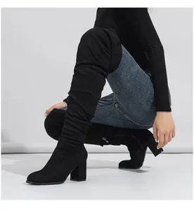 Close-up view of black suede over-the-knee boots with chunky high heel shown on a model