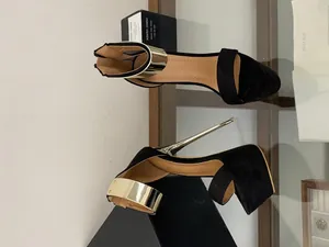 Detailed view of sexy black platform sandals with gold ankle cuff and high stiletto heel.