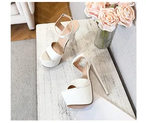 Elegant white platform sandals with stiletto heel and ankle strap on a wooden table