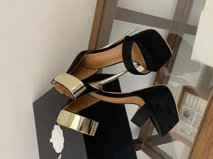 Macro detail of black suede platform sandals featuring gold metallic ankle straps and 16cm heels