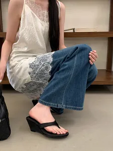 Detail shot of elegant black wedge thong sandals worn with denim jeans and lace dress