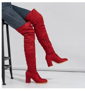 Side view of elegant red suede over-the-knee boots with chunky high heels on a model sitting.