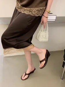 Detail view of elegant brown satin wedge flip-flop sandals worn with a chic dress