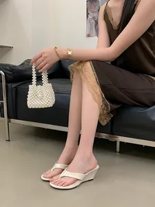 Elegant cream wedge thong sandals worn by a model sitting on a minimalist black sofa