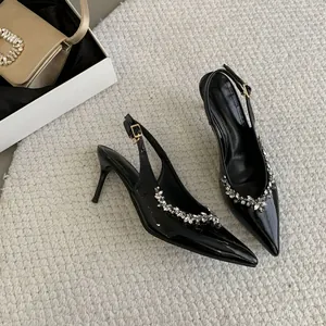 Detail der schwarzen Stilettos mit spitzer Kappe, Strassschnalle und Fersenriemen.
