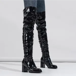 Full view of black shiny patent leather over-the-knee slouchy boots with chunky heels.