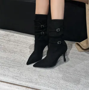 Close-up of black pointed-toe stiletto boots with buckle straps and pleated details