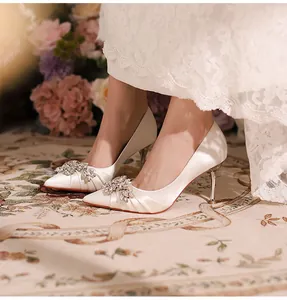 Detailed view of white satin pointed-toe high heels with elegant rhinestone buckle.