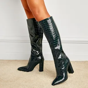 Detail of dark green crocodile embossed knee-high boots with pointed toe and block heel.