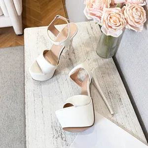 Elegant white platform stiletto sandals with ankle straps on a rustic white table