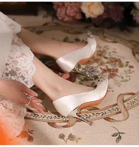 Close-up of white satin pointed-toe stiletto heels with a crystal buckle on a model