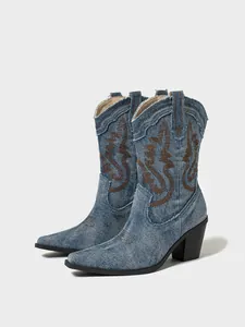 Close-up detail of blue denim Western cowboy boots featuring brown embroidery and block heel