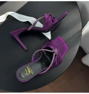 Elegant purple satin high-heeled sandals with sparkling rhinestone straps on black table