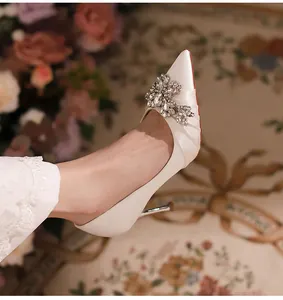 Close-up of white pointed-toe stiletto pump featuring a sparkling rhinestone flower detail