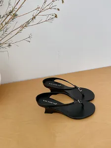 Detailed view of French minimalist black thong wedge sandals on a wooden surface.