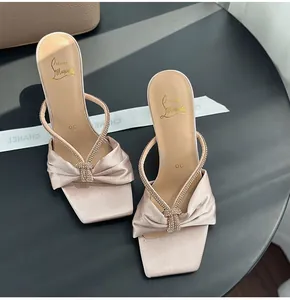 Close-up of pink satin heeled sandals featuring a sparkling rhinestone bow detail.