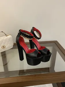 Detail of black platform sandals with chunky heels and gold chain ankle strap on glass table.