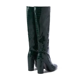 Detail of dark green crocodile-embossed knee-high boots with chunky high heels.