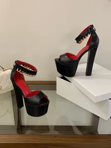 Detailed side view of black chunky platform sandals with gold chain on glass table