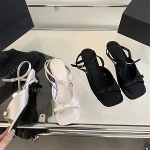 Detail view of French style high heel sandals with bows and ankle straps in black and white