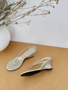 Close-up detail of minimalist champagne metallic wedge thong sandals on a wooden table