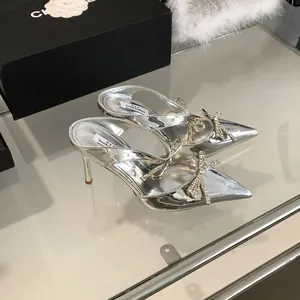 Detail shot of silver high-heeled sandals with rhinestone bow and pointed toe