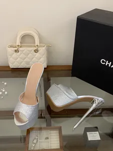 Silver glitter platform stiletto mules displayed on a glass table with props.