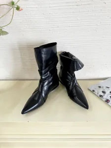 Close-up of stylish black pointed-toe short boots featuring elegant cross strap detail