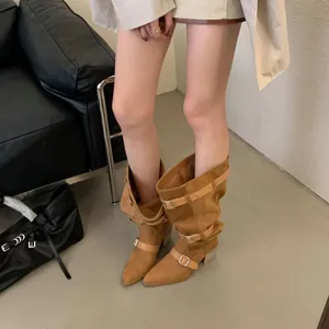 Detailed view of tan suede slouchy cowboy boots with buckle straps and pointed toe