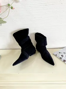 Detailed view of elegant black pointed-toe faux suede ankle boots in a lifestyle setting.