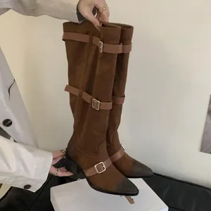 Detailed view of brown suede western boots with pointed toe and buckle straps.