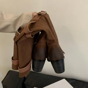 Detail of brown suede western slouchy boots with chunky heels and buckle accents.